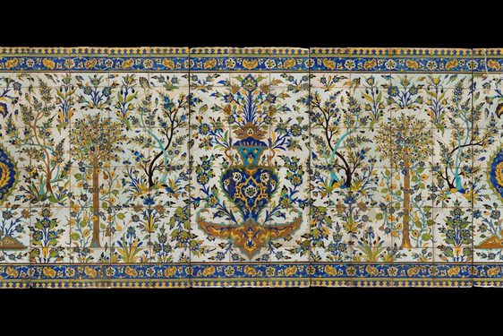 A long, rectangular panel made of hundreds of intricately decorated, painted tiles. This image gives the overall impression of the illustration, which from a distance is of a garden scene with trees all around, and a fountain as the centrepiece. The colours painted are yellow, blue, green and brown.