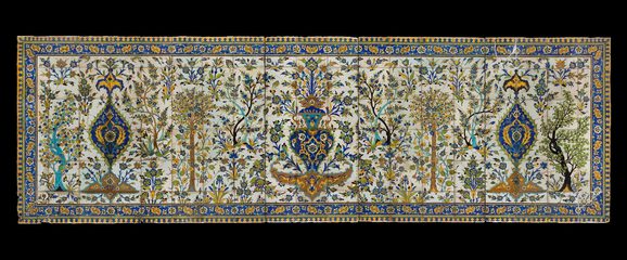 A long, rectangular panel made of hundreds of intricately decorated, painted tiles. This image gives the overall impression of the illustration, which from a distance is of a garden scene with trees all around, and a fountain as the centrepiece. The colours painted are yellow, blue, green and brown.