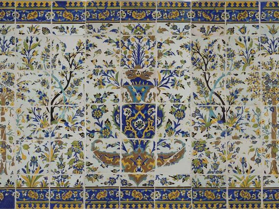 A long, rectangular panel made of hundreds of intricately decorated, painted tiles. This image gives the overall impression of the illustration, which from a distance is of a garden scene with trees all around, and a fountain as the centrepiece. The colours painted are yellow, blue, green and brown.
