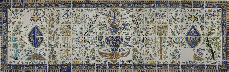 A long, rectangular panel made of hundreds of intricately decorated, painted tiles. This image gives the overall impression of the illustration, which from a distance is of a garden scene with trees all around, and a fountain as the centrepiece. The colours painted are yellow, blue, green and brown.