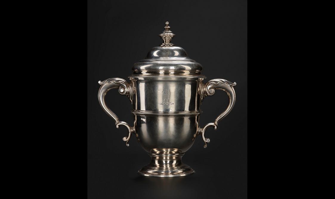 A silver trophy cup with two handles either side and a lid on top