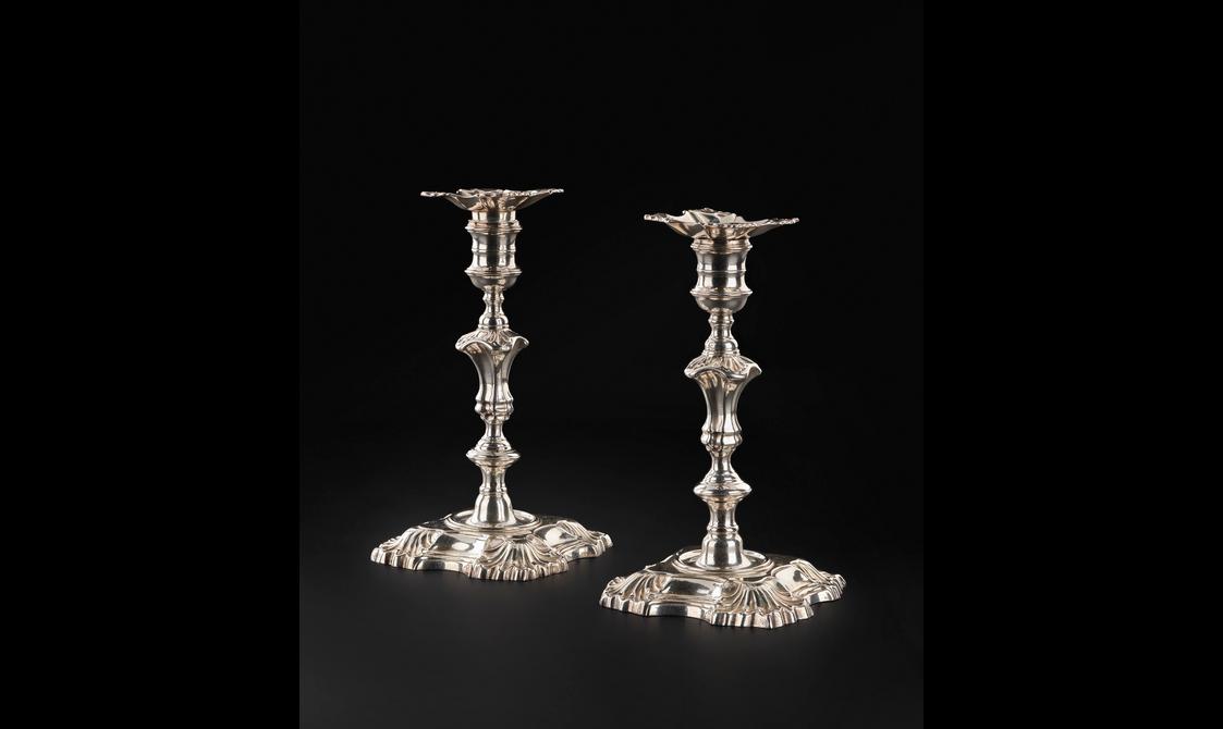 A pair of ornate silver candle sticks against a black background