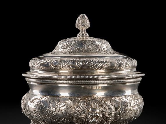 An ornate silver sugar bowl with three short legs and a lid