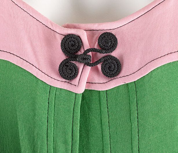 Detail of a pink and green dress with a black spiral toggle at the chest.