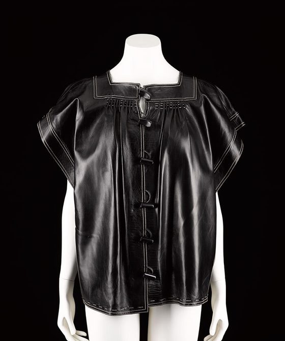 A mannequin wearing a short sleeved black leather tuni top with fastenings down the front.
