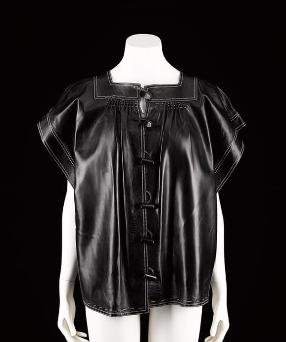 A mannequin wearing a short sleeved black leather tuni top with fastenings down the front.