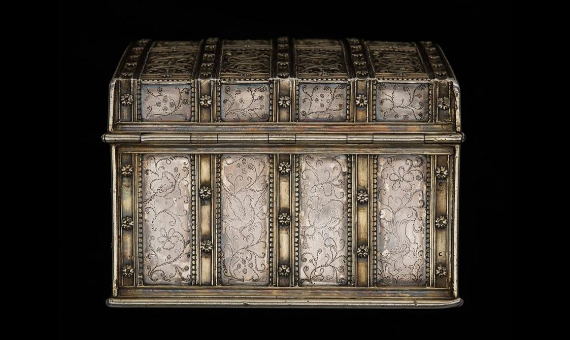 Side of the ribbon-like strap work silver casket decorated with flowers and pin pricked bird and branch motifs.