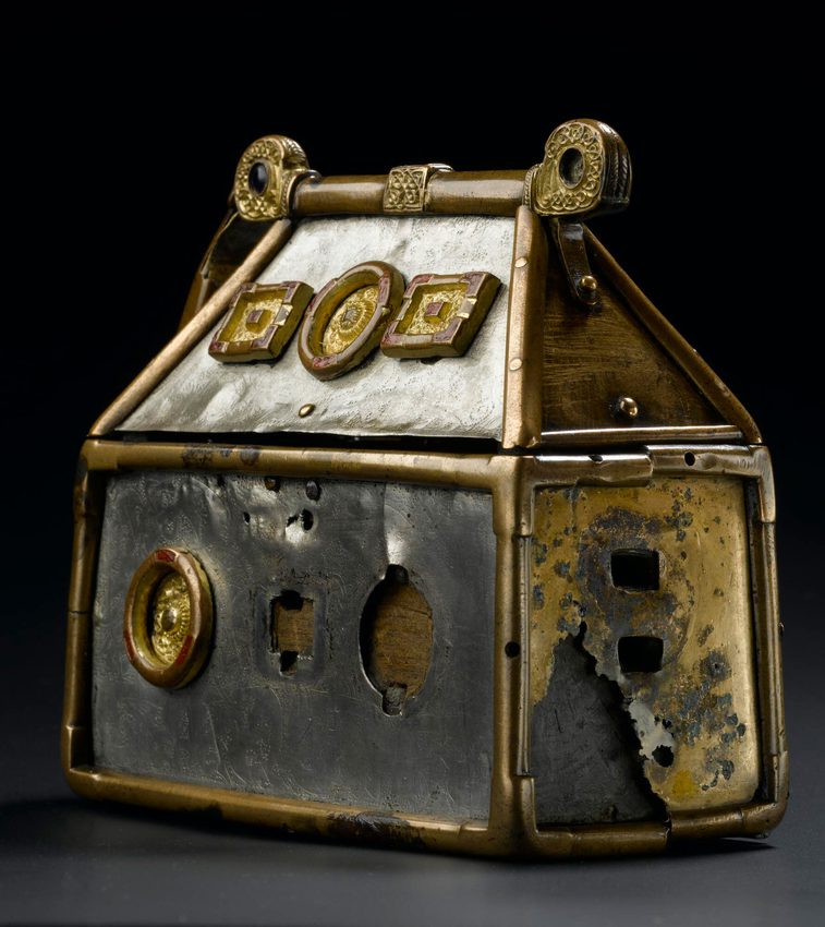 A small silver box with gold metalwork on the edges. In view is a damaged copper side plate revealing wood underneath.