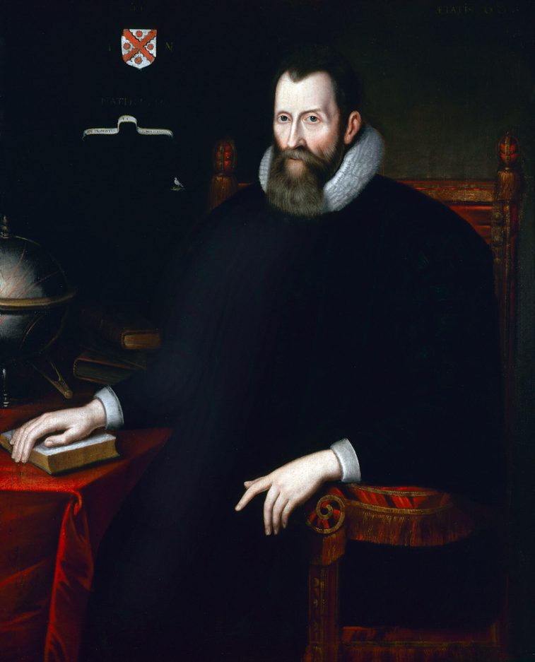 A dark colour painting of a pale-faced man wearing black and white collar ruff. He is sitting on a red-cushioned chair and has his right hand resting on a book on a table covered in red cloth.