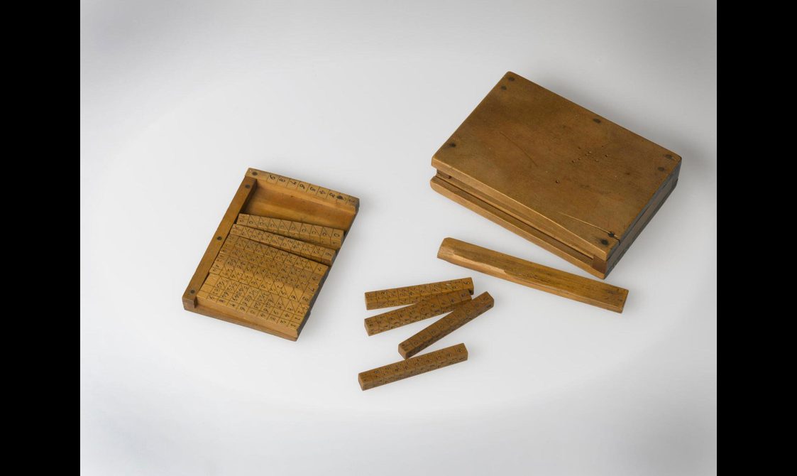 A colour photograph of a wooden box and wooden rods. The part of the box on the right contain many rods with engraved numbers.
