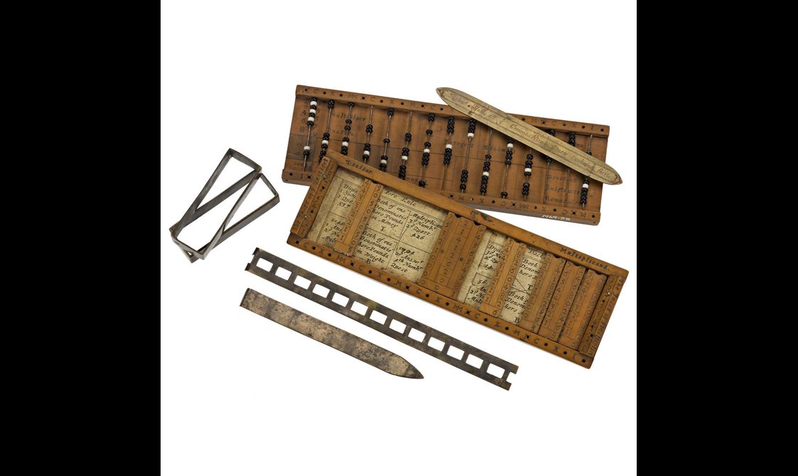 A colour photograph of a set of wooden devices including a bead abacus, a rule, a wooden frame with some inserted text.