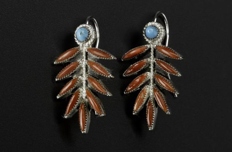 A pair of long silver earrings with turquoise circles and coral leaf like shapes photographed against a black background