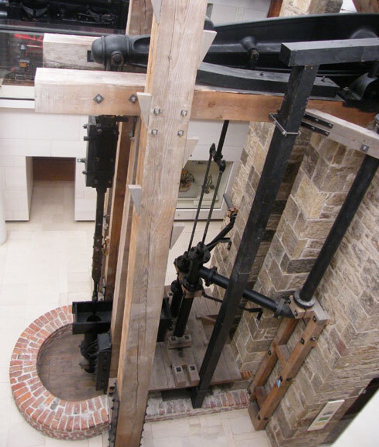 A large engine made of steel supported by wooden beams attached to a brick building.