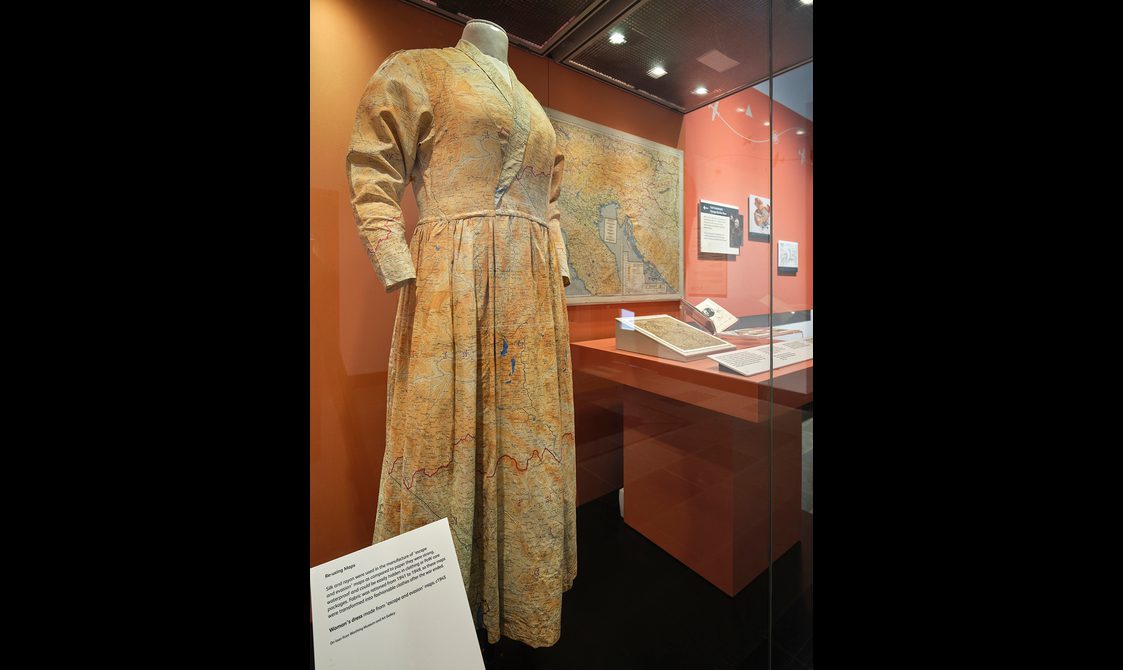 A long sleeved midi dress made out of silk maps on display in a glass case