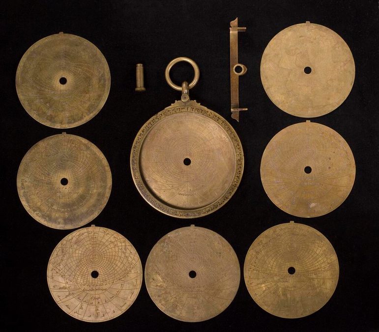 An unpacked version of the astrolabe showing all of its bronze components, including seven circular plates, the back of the main body, a central pin and a sighting vane.