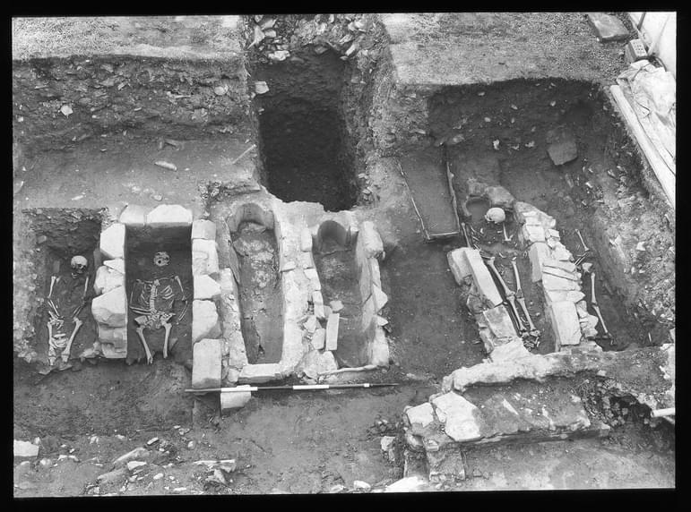 Black and white photograph of a burial site, with excavated graves and skeletons.