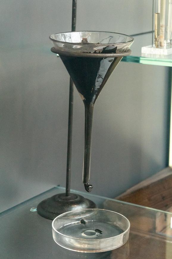 A glass funnel filled with a thick black substance suspended over a petrie dish.