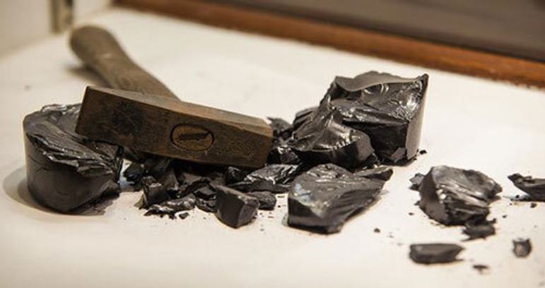 A white table with broken up pieces of a black shiny rock and a hammer