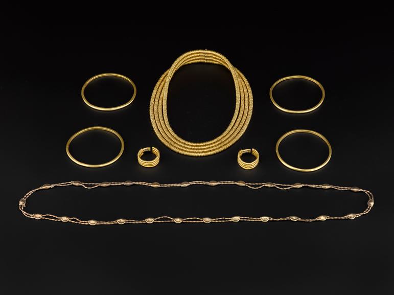 A collection of gold jewellery including four bangles, two necklaces, and a set of earrings set against a black background