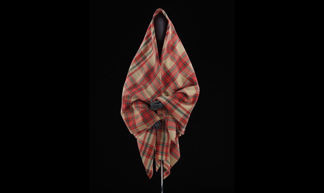 A mannequin wearing a red and cream tartan shawl.