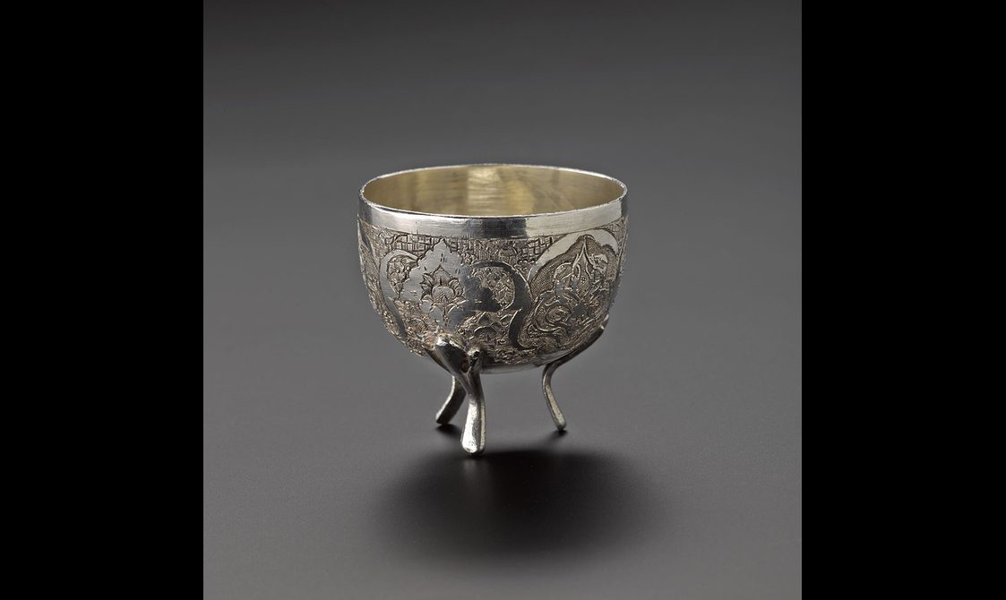 A small silver bowl with highly decorated surface, standing on three legs.