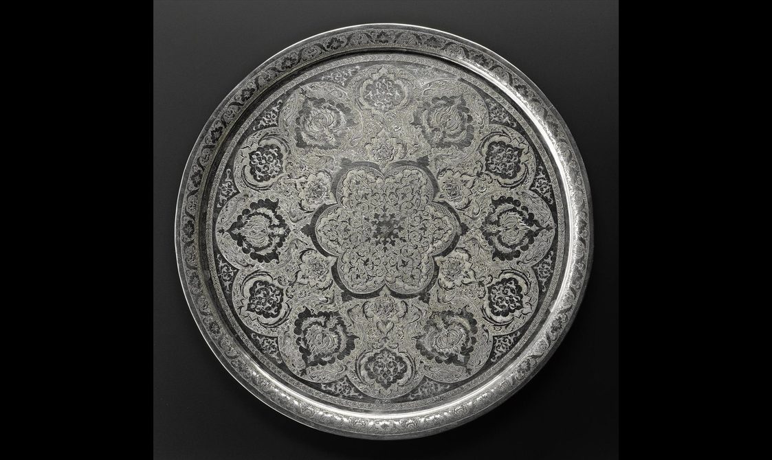 A circular silver tray with floral motifs engraved on its surface.