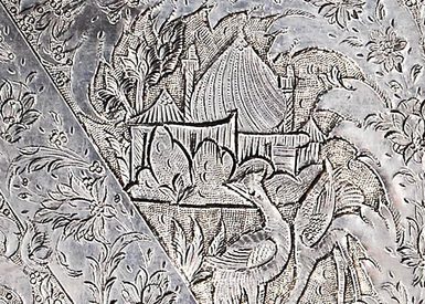 Detail of a silver object with flowers, a mosque, and a minaret engraved on its surface.