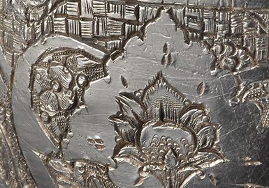 Detail of a silver object with floral pattern.