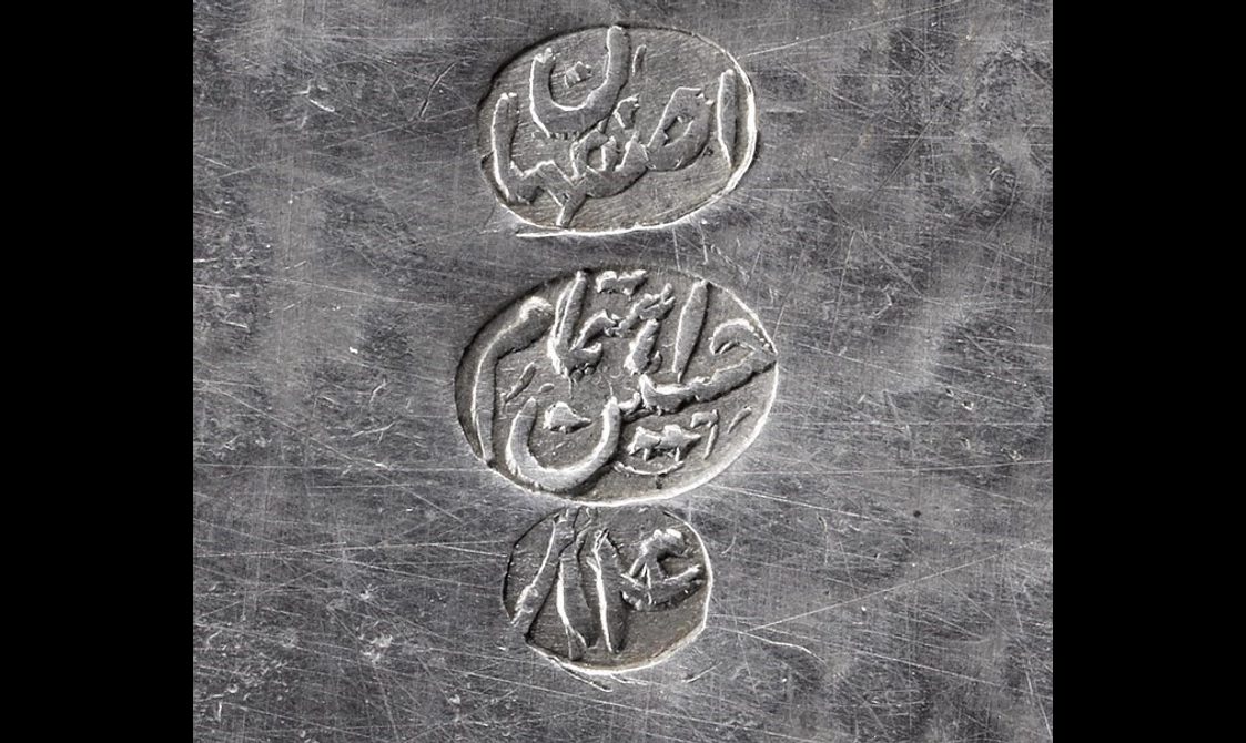 Detail of a silver object showing three marks to indicate the maker.