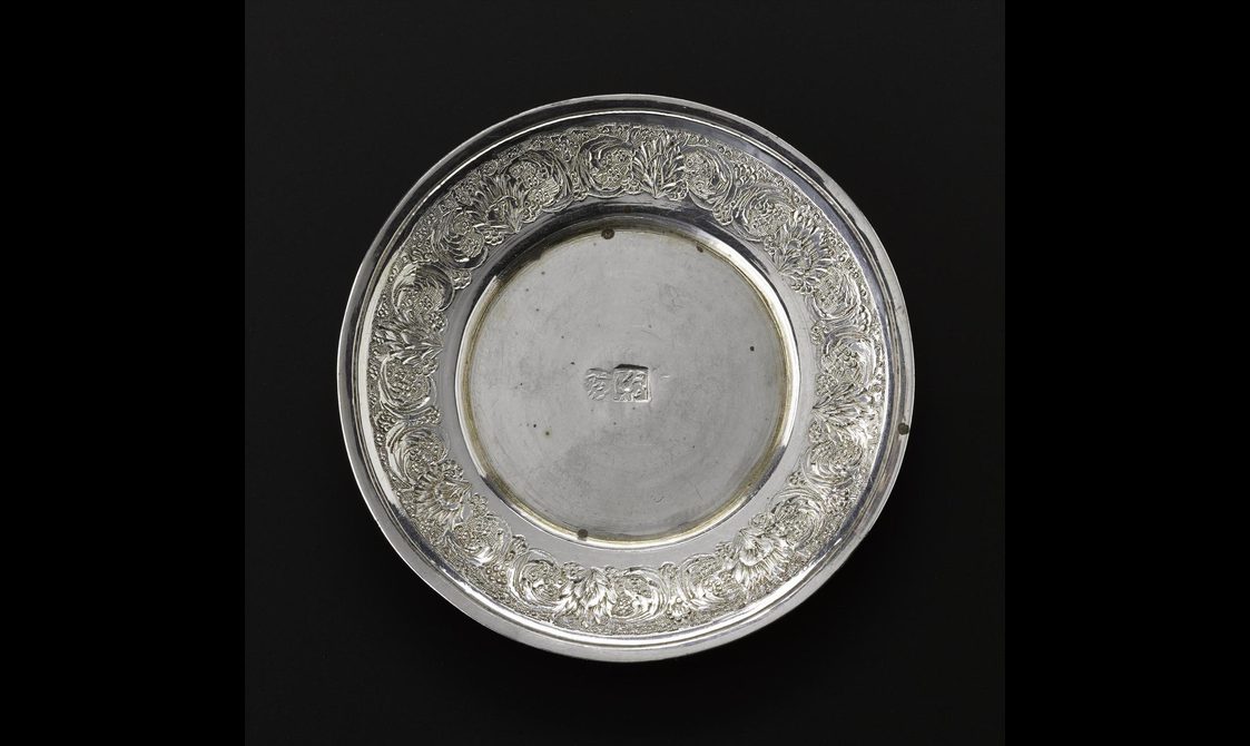 Miniature silver saucer with floral decoration around the outside rim and hallmarked in the centre.
