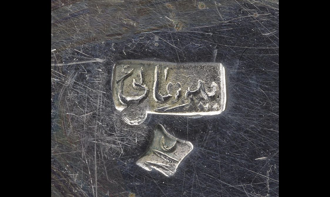 A detail of a silver object with two stamps to indicate the maker.