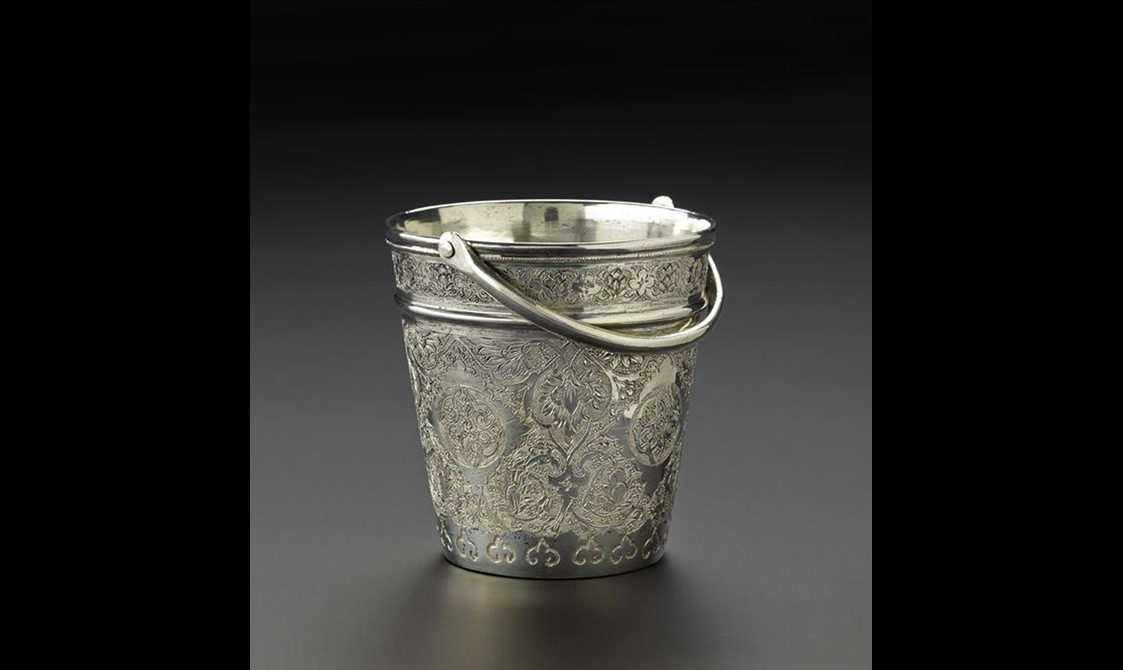 A silver ice bucket with floral patterns engraved all over the surface.