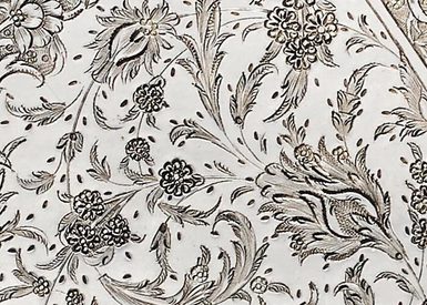 Detail of a silver object with an engraved floral pattern.