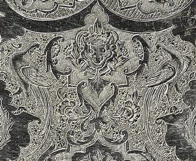 Detail of a round silver object with detailed floral patterns engraved on its surface.