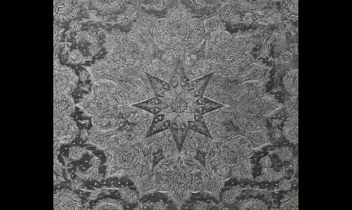Detail of a silver object with a star pattern and fine details engraved all over the surface.