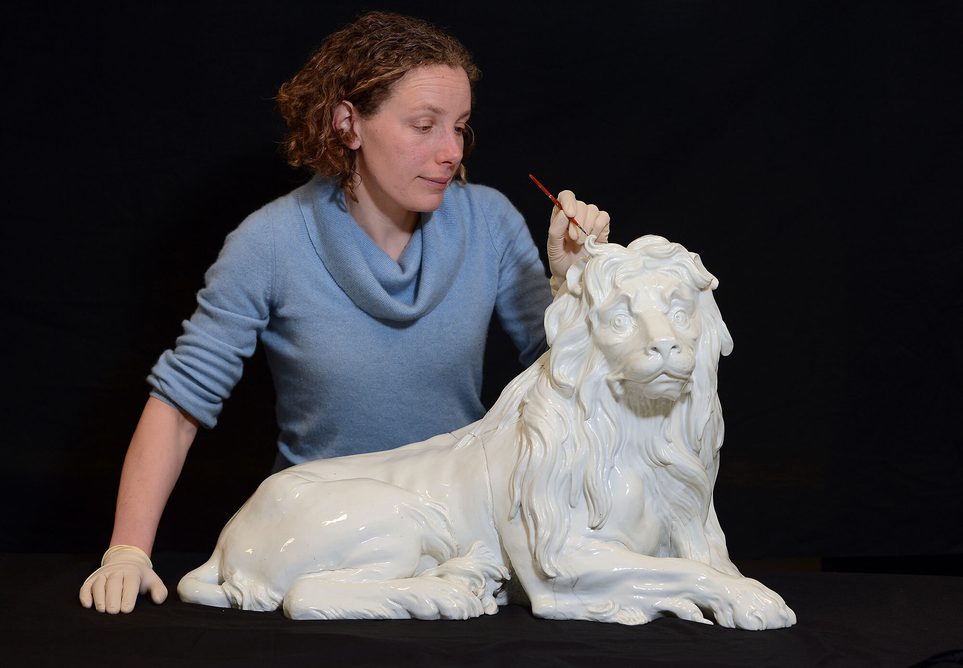 A conservator using a small brush to repair a porcelain lion figure