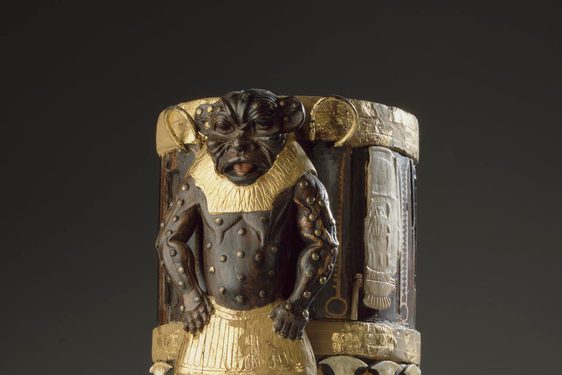 A cylindrical box made of wood, gold, and ivory with decorative elements including a lion-like figure.