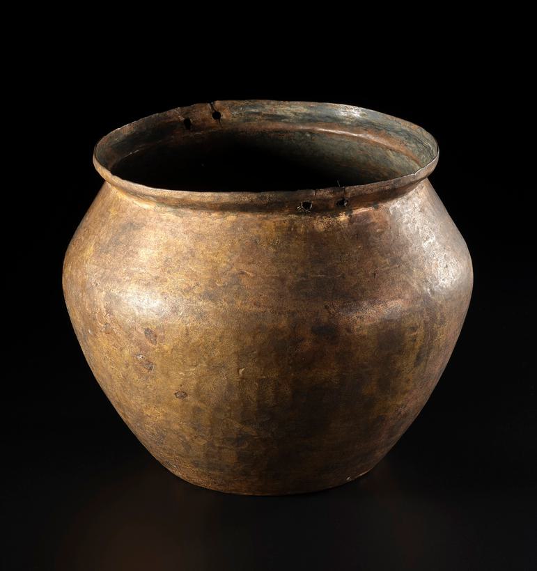 A wide pot, yellow-brown in colour standing upright against a black background.
