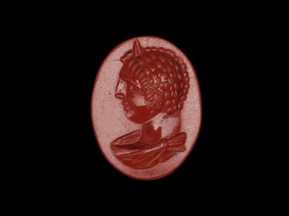Small red gemstone that looks almost like a wax seal. Egg-shaped, with a male figure sporting right curls and large nose in profile facing left.