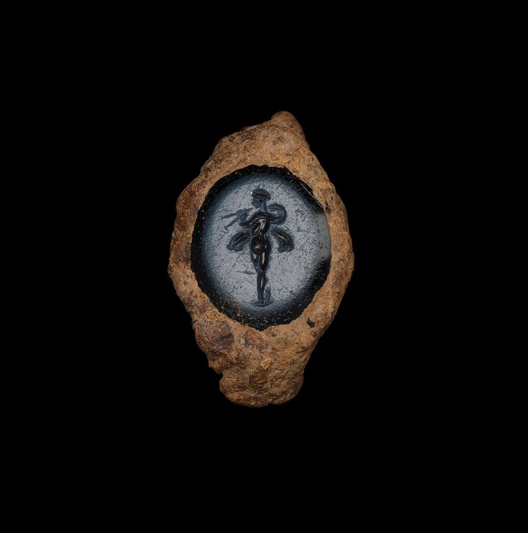 A gemstone of grey-blue set within a badly rusted ring. An elegant figure in black stands within, poised like a dancer.