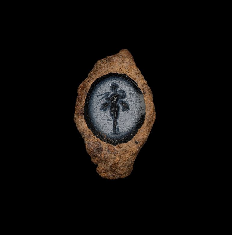 A gemstone of grey-blue set within a badly rusted ring. An elegant figure in black stands within, poised like a dancer.