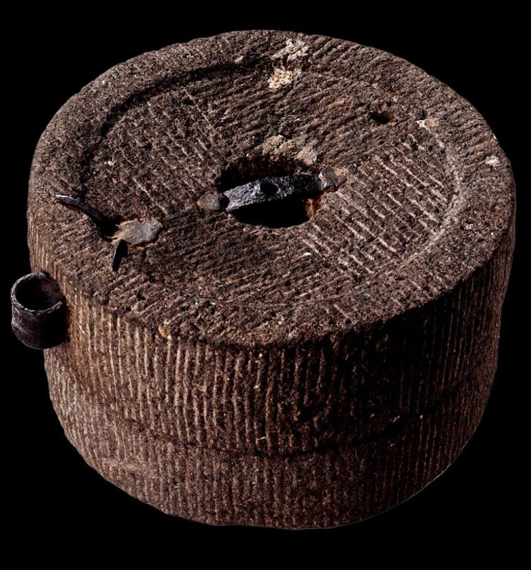 Two brown quernstones one atop the other. Perfectly round, with a regular but coarse-looking surface of lines making it resemble a loaf of burnt bread.