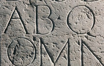 Smooth, grey stone surface with large carved Latin letters across it in regular rows.