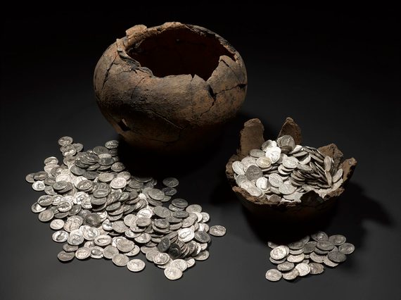 On left, a large, empty dark brown pot missing its lid with a pile of silver coins in front of it. On right, the basin of another container filled with silver coins.