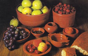 Eight terracotta-coloured dishes on a table, overflowing with grapes, apples, other fruits and bread like a cornucopia.