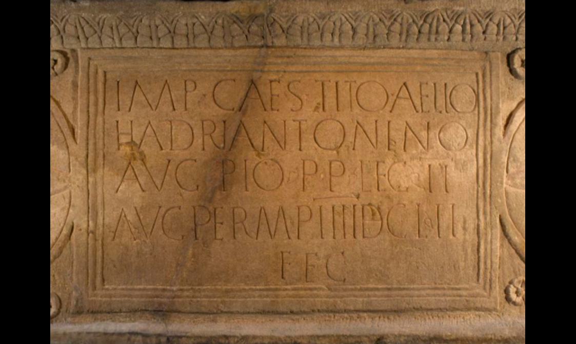 Close-up of an orange stone slab with Latin text written in neat rows across its whole surface.
