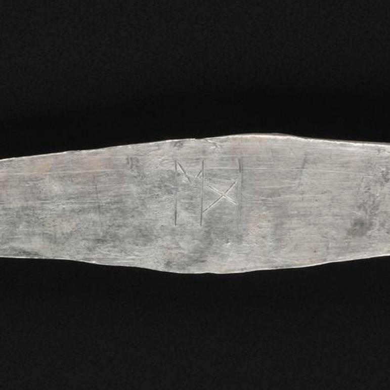 A close up of an inscription on the arm band, which looks like the letter M.