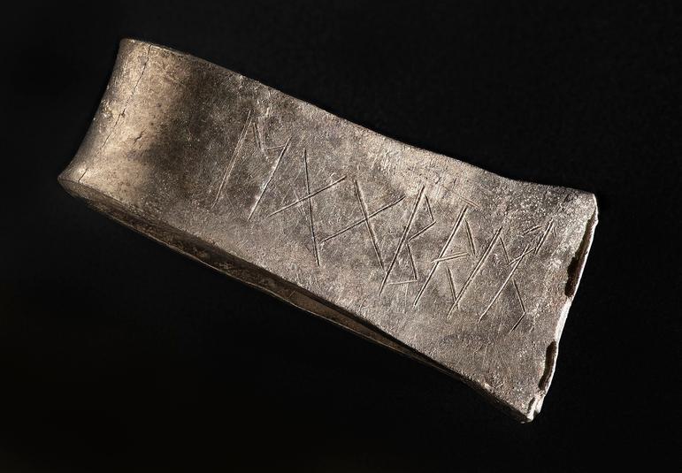 A close up of the flat surface of an arm band, which shows a clearly engraved runic inscription.
