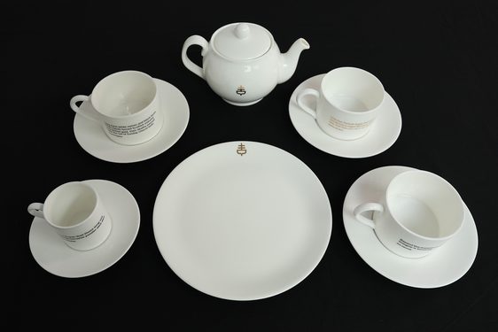 A white tea set of four cups and saucers, a teapot, and a serving plate
