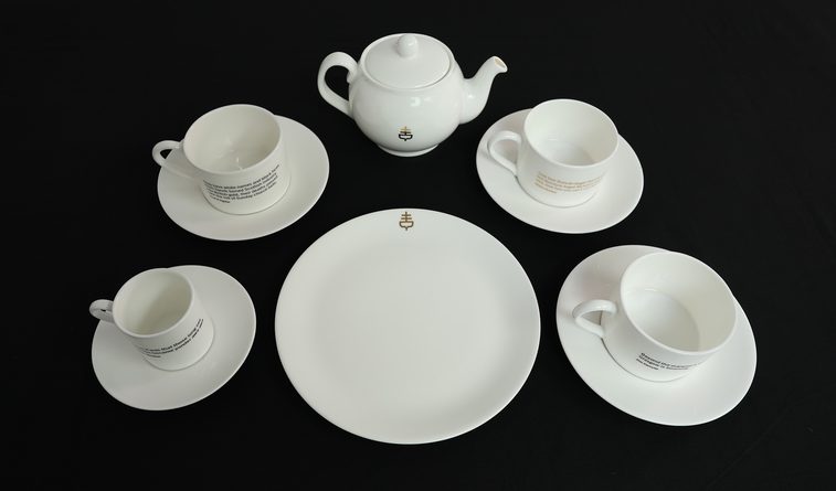 A white tea set of four cups and saucers, a teapot, and a serving plate